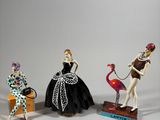 three figurines of people dressed in costumes and holding flamingos