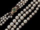 three strand pearl necklace with emerald clasp on a black background