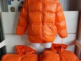 une veste orange posée sur un présentoir à mannequin, à côté d'une paire de coussins