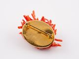 yellow and red broochi pin with red corals on a white surface
