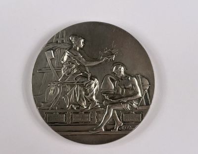 une photo représentant une médaille d'argent sur laquelle figurent une femme et un homme assis sur un banc