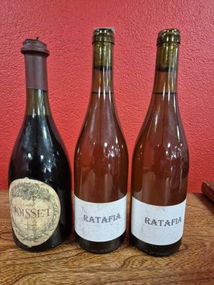 three bottles of wine sit on a wooden table in front of a red wall