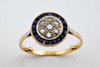gros plan d'une bague en or avec des pierres bleues et blanches