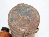 a rusted metal container with a lid next to a bottle