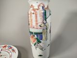 a white vase with a painting on it next to a plate