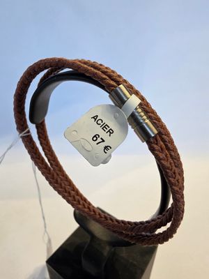 bracelet en cuir marron muni d'un fermoir en métal, présenté sur un présentoir noir