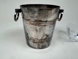 a metal bucket with handles and a glass on the table
