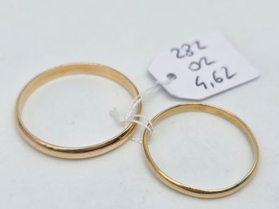 two gold wedding rings on a white surface with a price tag