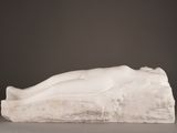 sculpture of a woman laying on a rock on a gray surface