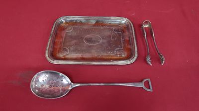 a silver tray with a spoon, spoon and spoon rest on a red table cloth