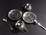 three silver teapots and two silver spoons on a black table
