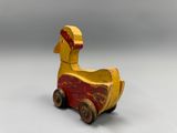 yellow and red wooden toy duck sitting on top of a white surface