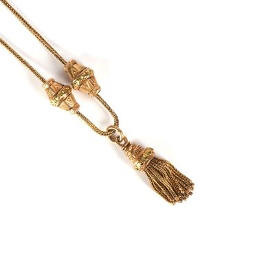 a close up of a gold necklace with a tassel on a white background