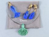 une paire de boucles d'oreilles bleues et dorées ornées d'un pompon, présentée dans une pochette