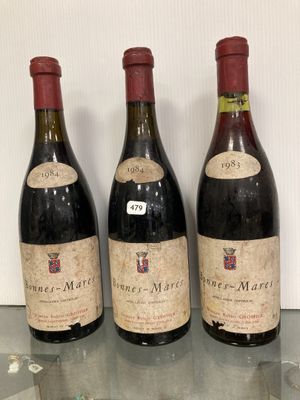 trois bouteilles de vin posées sur une étagère en verre, à côté d'une bouteille de vin