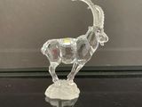 une figurine de chèvre en cristal posée sur une table en verre