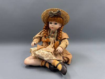 poupée assise par terre, coiffée d'un chapeau de paille et vêtue d'une robe