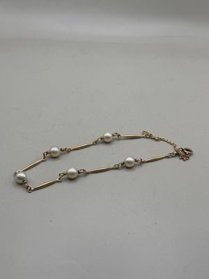 a gold chain bracelet with pearls on a white background