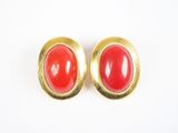 une paire de boucles d'oreilles rouges et dorées posées sur une surface blanche