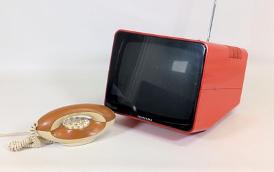 un petit téléviseur orange et un téléphone posés sur un plan de travail blanc