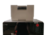 a person taking a picture of a microwave with a printer on top of it