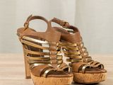 gold strappy platform sandals on a wooden table with a curtain in the background