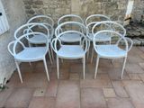 six white plastic chairs sitting in front of a stone wall