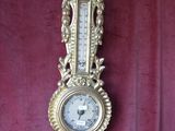 a gold clock hanging on the wall with a red curtain in the background