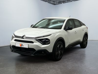 Une voiture blanche est garée dans une pièce blanche au sol noir.