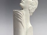 sculpture of a woman ' s head on a white vase on a gray background