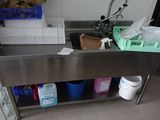 un évier en inox dans une cuisine où l'on trouve beaucoup de produits d'entretien