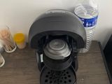 a black coffee maker on a wooden table next to a bottle of water