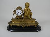 une horloge dorée posée sur un socle noir, ornée d'un chérubin