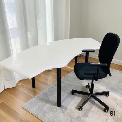 un bureau blanc avec une chaise noire devant une fenêtre