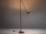 un lampadaire noir posé sur une surface blanche, dont la lampe est allumée
