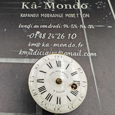 horloge avec des chiffres romains, exposée devant une enseigne « ka - mondo »