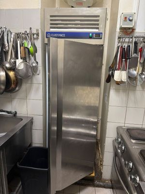 un réfrigérateur en acier inoxydable dans une cuisine où des casseroles et des poêles sont accrochées au mur