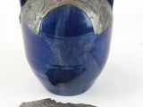 un vase bleu et un morceau de métal posés sur une surface blanche