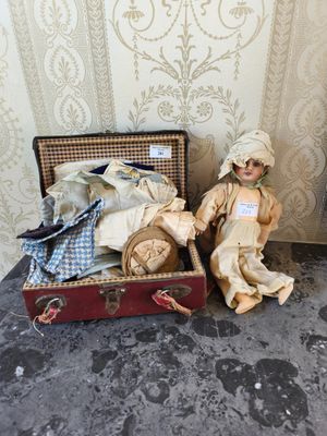 une poupée assise dans une valise à côté d'une autre poupée