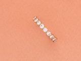 une bague simple en forme de barre, ornée d'une perle et d'un diamant, sur fond couleur pêche