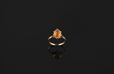 a gold ring with an orange stone on a black surface