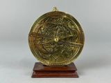 a close up of a brass clock on a wooden stand