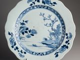 blue and white plate with flowers and birds on it on a stand