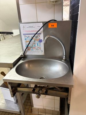 un lavabo dans des toilettes publiques, avec une affiche accrochée au mur