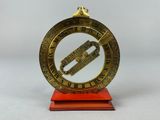 une vieille horloge en laiton posée sur un socle rouge, avec des chiffres romains
