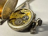a silver pocket watch sitting on a table next to a pen