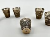 six silver shot glasses and a silver shot glass on a white surface