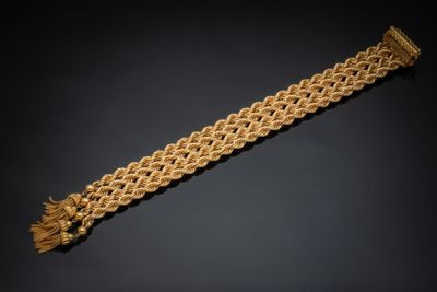 a gold bracelet with fringes on a black background