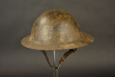 un vieux casque militaire posé sur un socle, sur fond gris