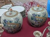 deux vases posés sur une table où se trouvent des assiettes et des tasses